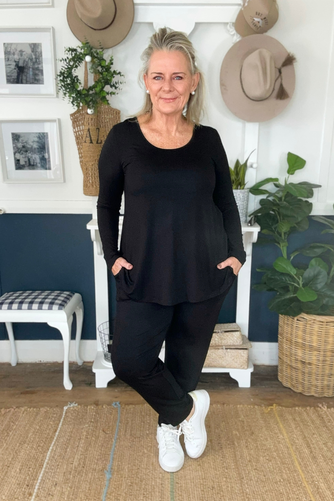 A woman wearing black bamboo trousers with an elastic waistband and tapered leg, paired with a relaxed black Margot top and white sneakers.