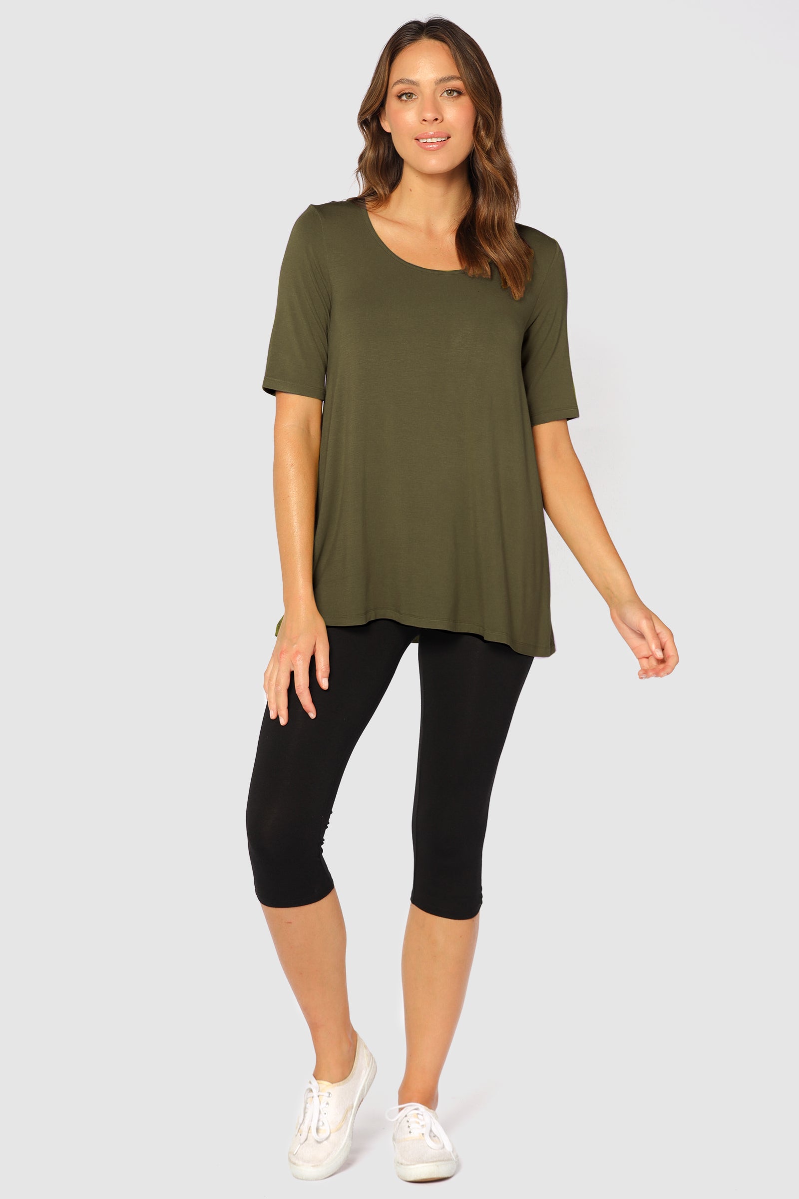 A woman wearing mid-rise black 3/4 leggings with a soft fabric waistband, paired with a green tunic top