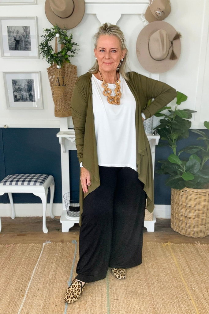 a mature woman wearing wide leg bamboo pants in black colour paired with the khaki waterfall cardigan and a relaxed white top