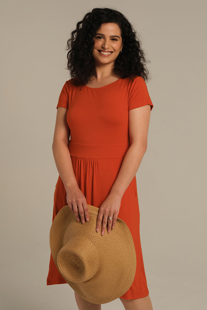 Woman wearing a knee-length orange bamboo dress while holding a wide brimmed hat