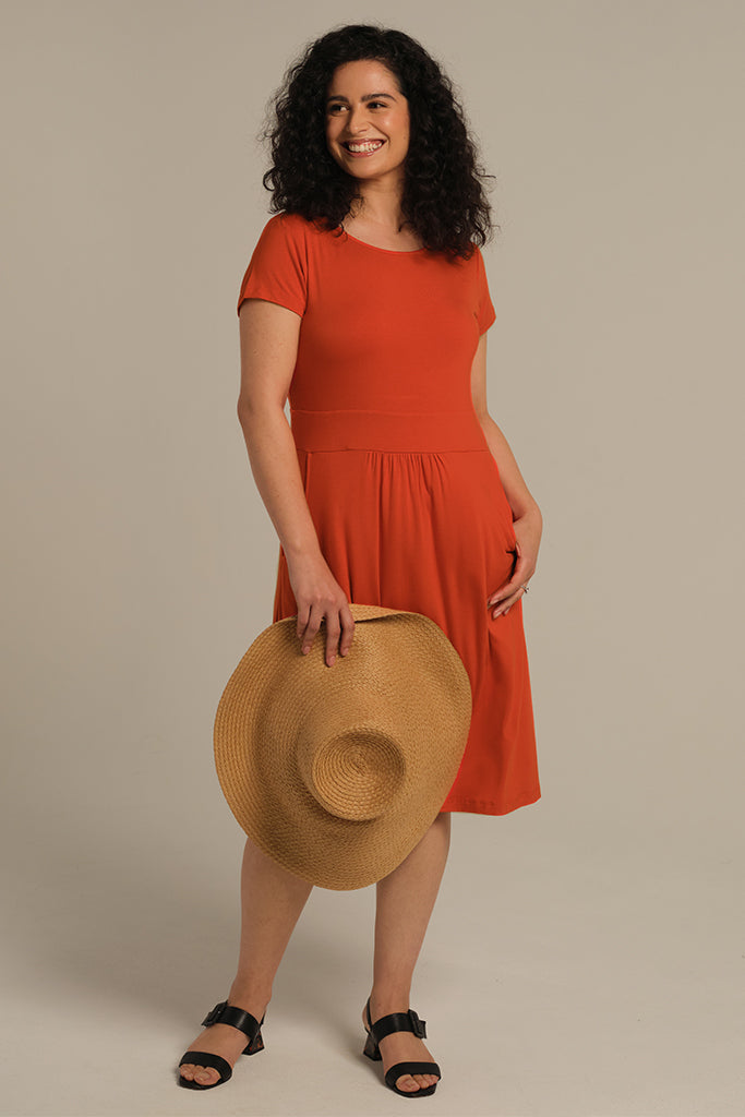 Woman wearing a casual orange dress for summer, featuring an in-built waistband and pleat detailing.