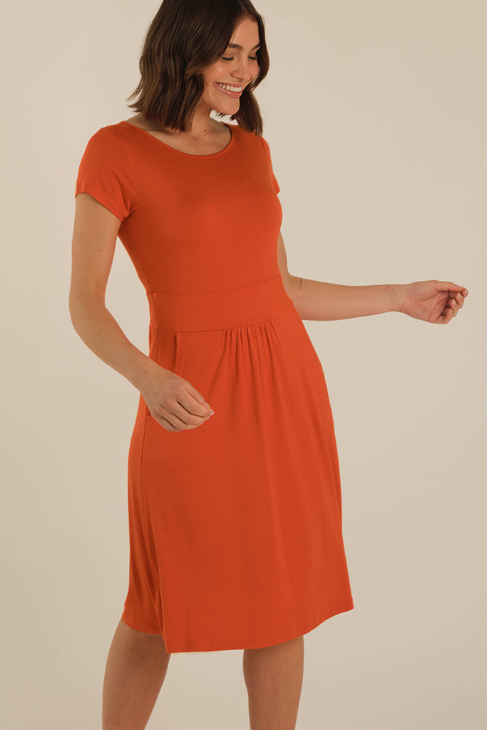 Model wearing a lightweight summer dress in orange with side pockets, waistband and short sleeves.