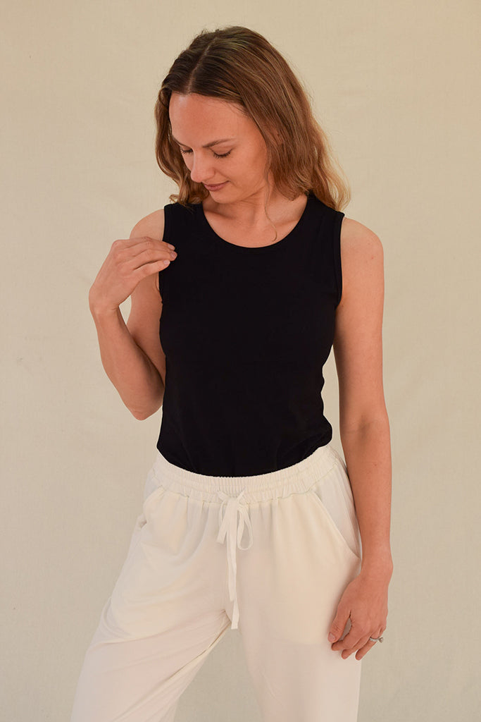 Woman wearing a black sleeveless top and white pants against a beige background