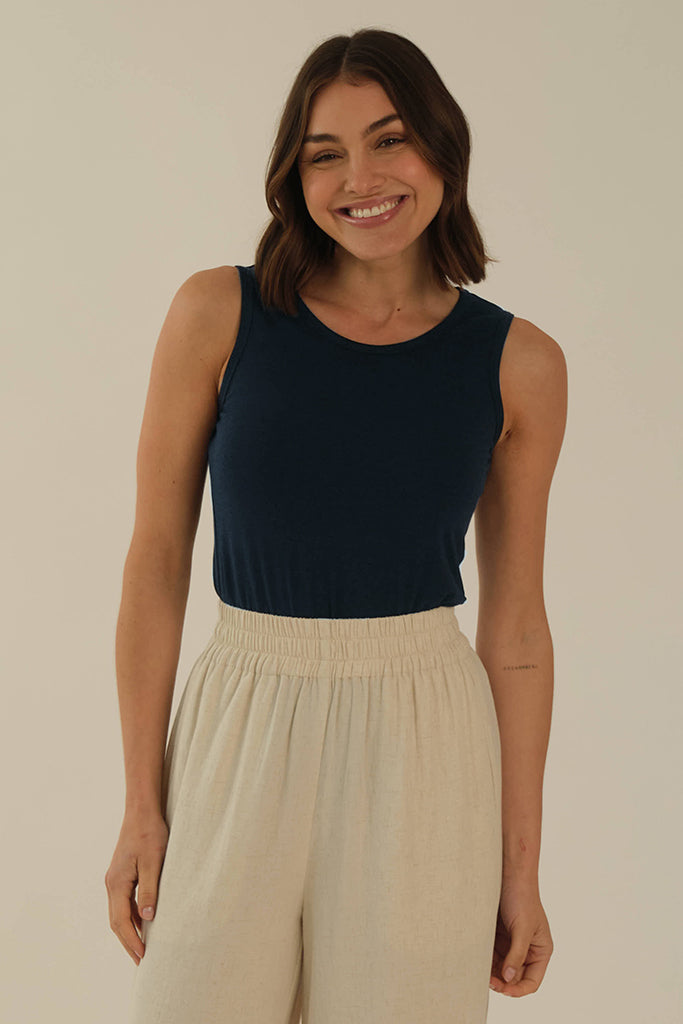 A female model wearing a dark navy sleeveless singlet with a high scoop neckline and thick straps.