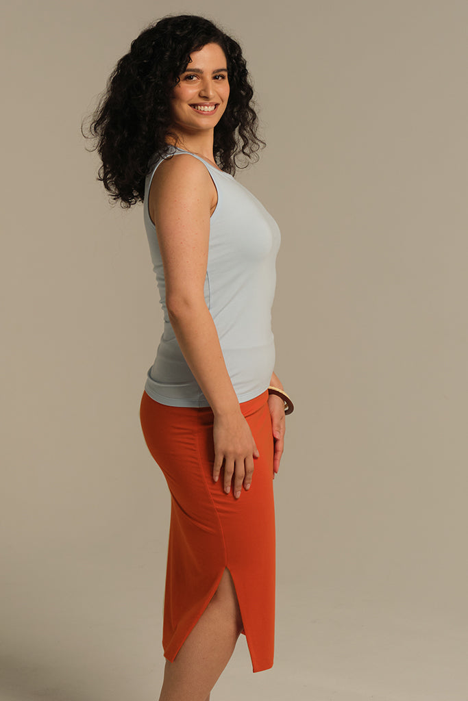 Side view of a model wearing a fitted baby blue singlet paired with an orange skirt.
