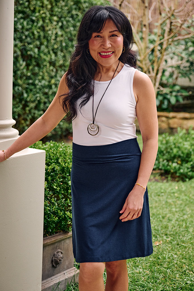 Model wearing a fitted scoop singlet in white paired with a dark navy knee length skirt.