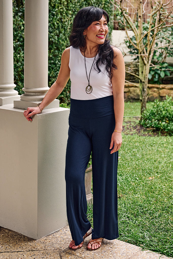 Model in a white sleeveless bamboo singlet and navy pants standing outdoors.