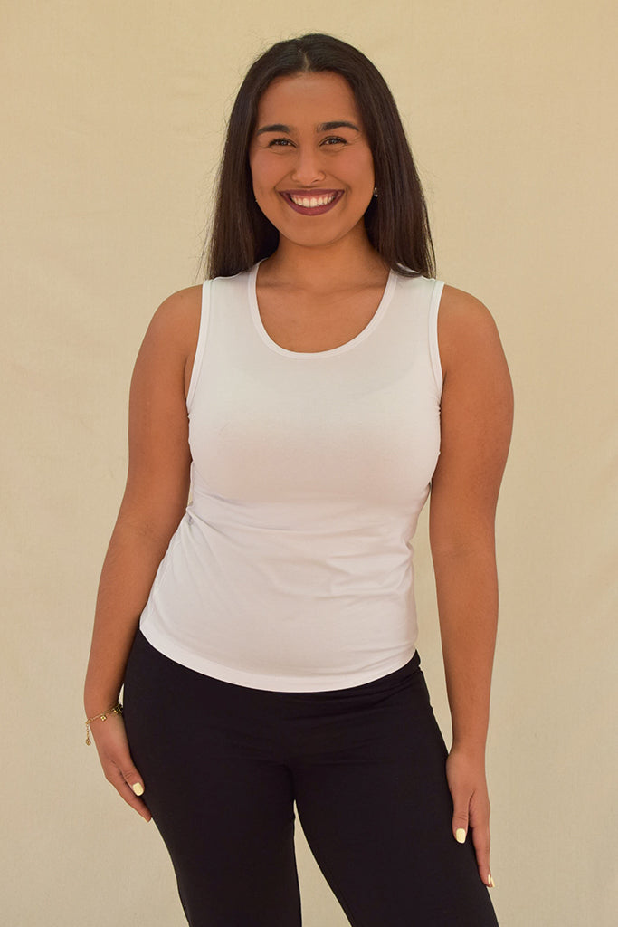 Woman wearing a white tank top and black pants against a beige background