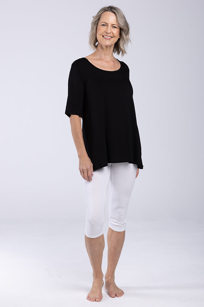 A mature woman wearing mid-rise white 3/4 leggings with a soft fabric waistband.