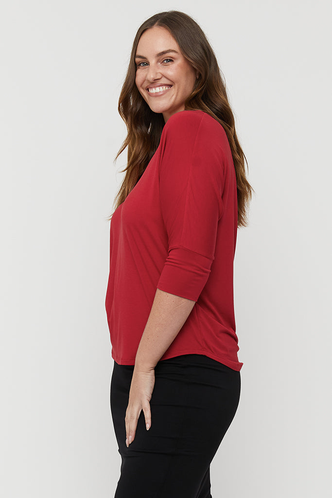 Side view of model wearing a loose red tee with 3/4 length sleeves.