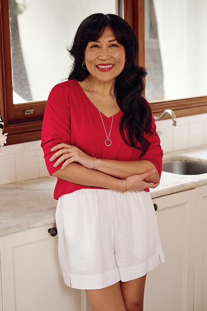 Model crossing her arms and smiling while wearing a red v neck tee with 3/4 cuffed sleeves tucked into white shorts.
