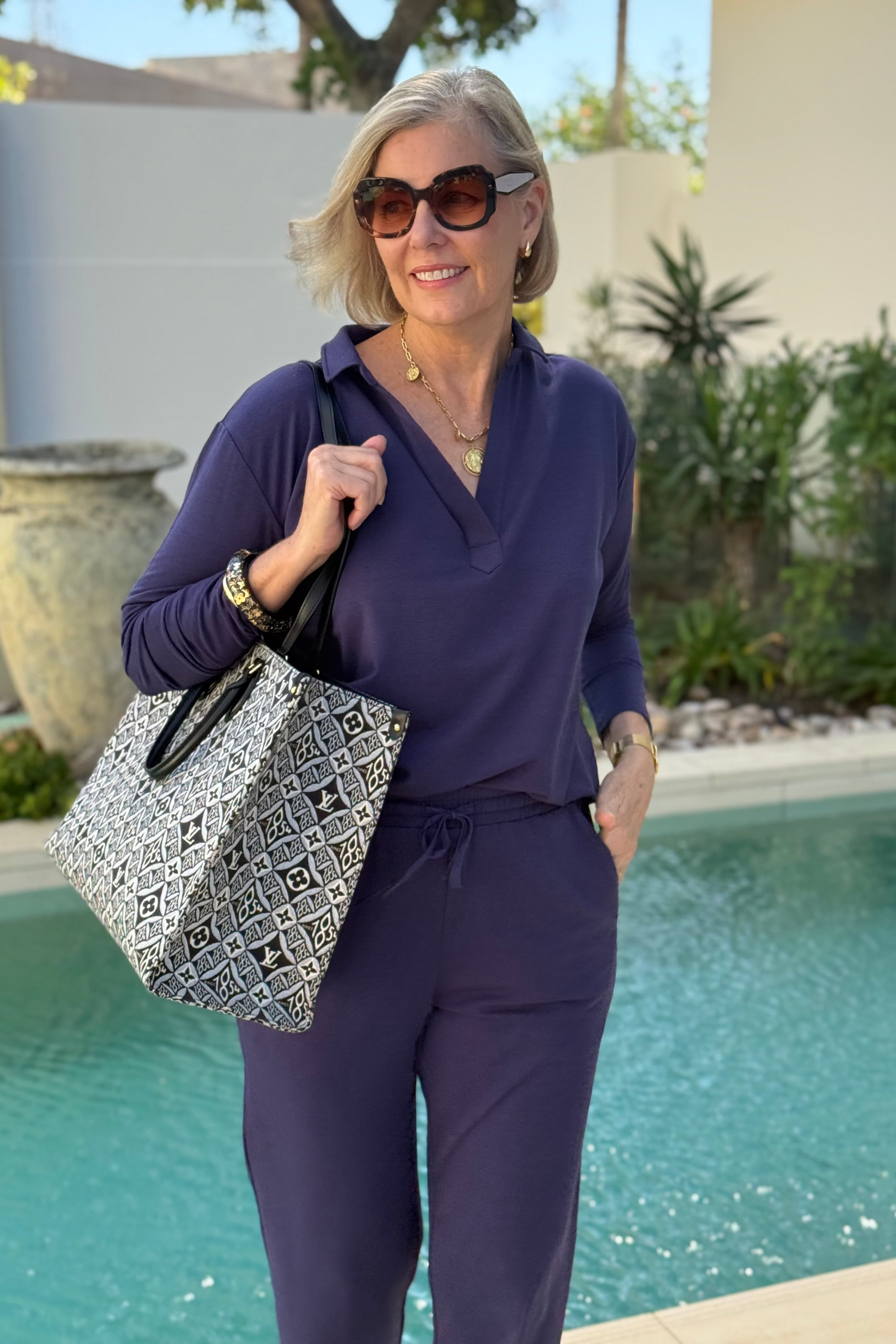 Woman in a purple outfit holding a patterned bag by a pool