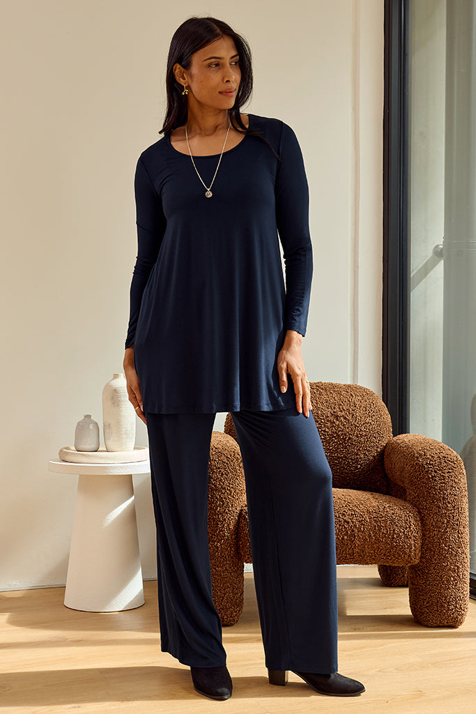 Woman wearing a navy blue outfit standing in a room with a brown armchair and white wall.