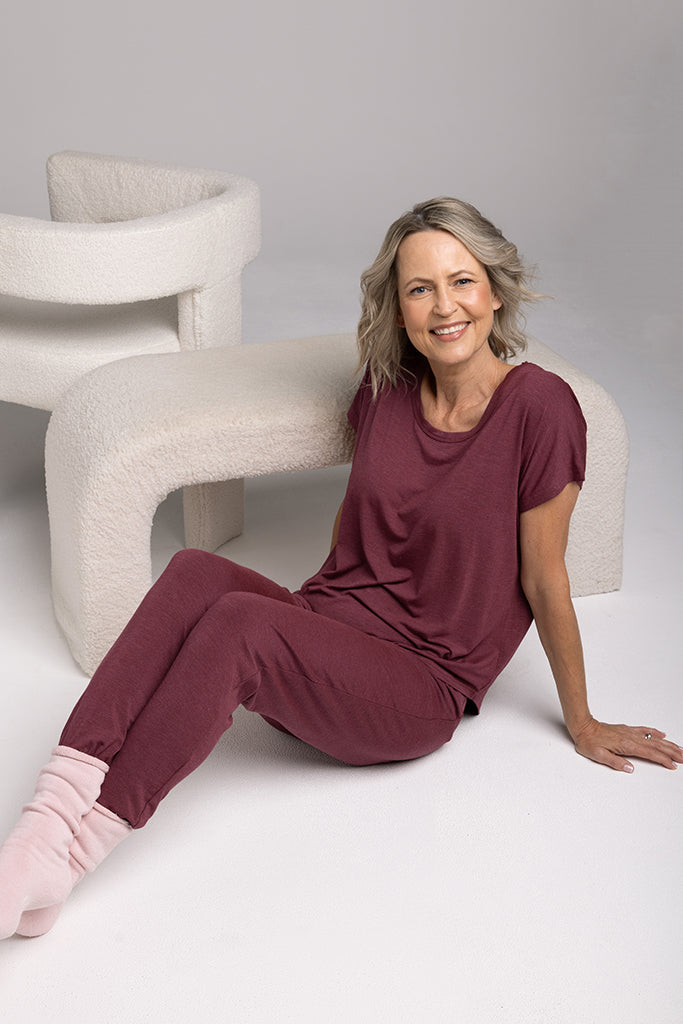 Model sitting in a relaxed posture wearing a relaxed, oversized burgundy pyjama top and matching bottoms.