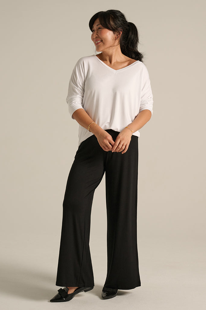 A woman models a pair of Luxe Wide Leg Pants in black, paired with a white top, showcasing a comfortable and stylish silhouette.