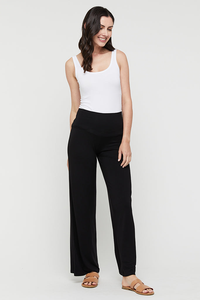 A woman wearing a white tank top and black wide-leg pants with a wide fabric waistband.