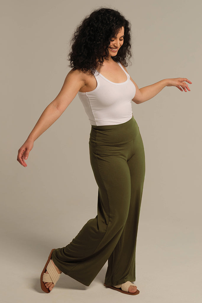 A woman modeling dark olive wide leg pants with a wide fabric waistband, paired with a white top