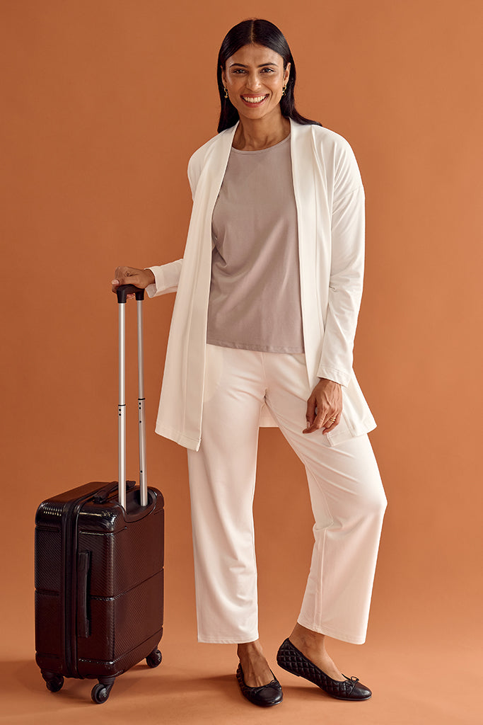 Woman in a white travel outfit with a suitcase on an orange background