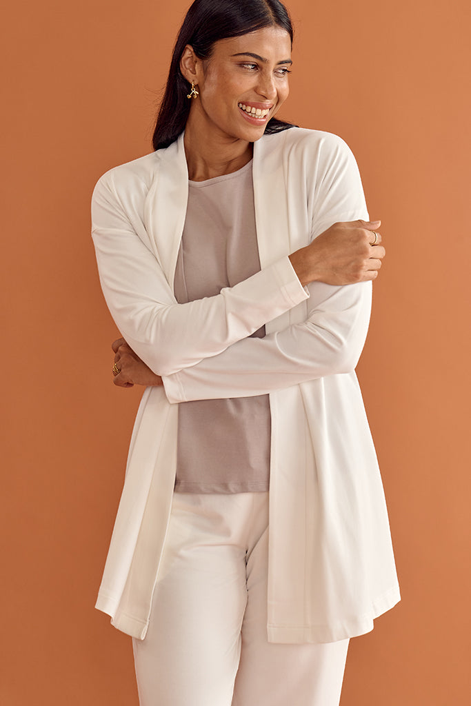 Woman wearing a white bamboo cardigan over a beige top and pants on an orange background