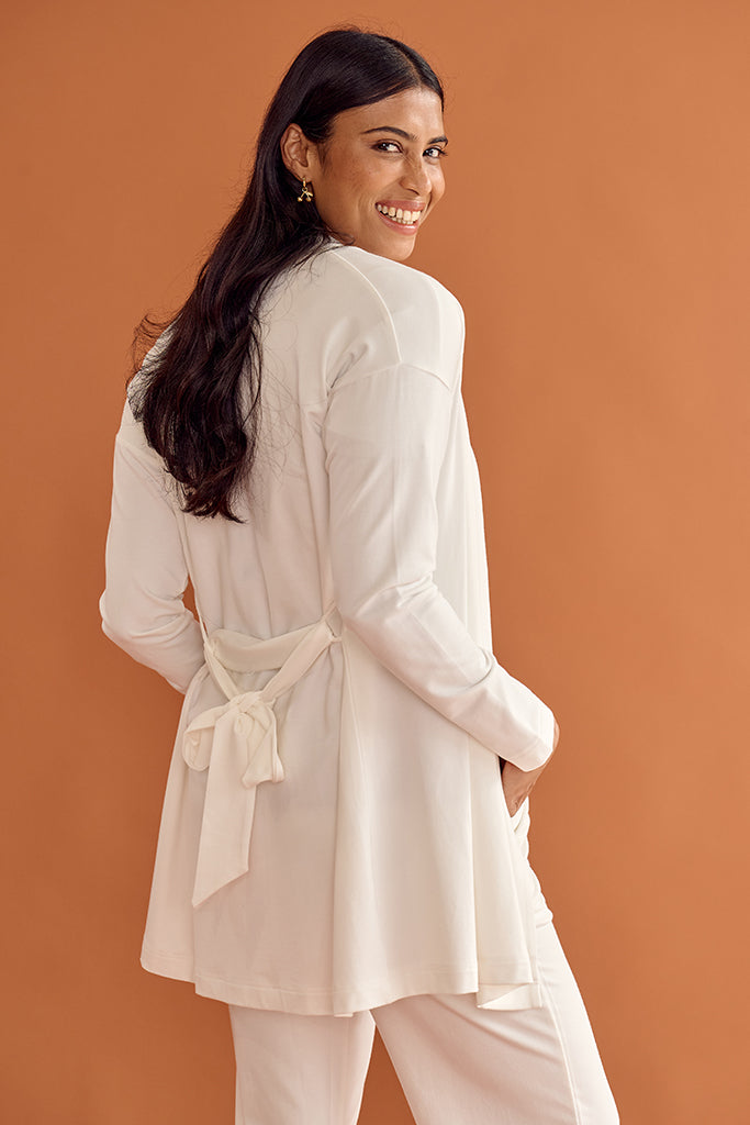 Close up of woman wearing a white Cardigan with a belt against an orange background