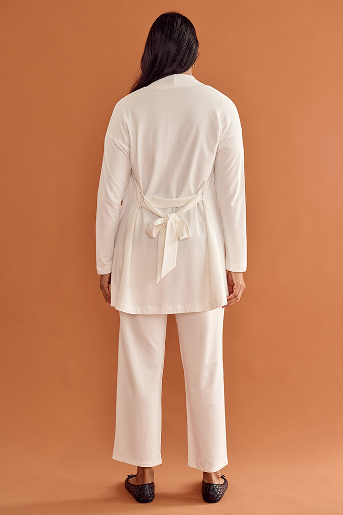 Model wearing a white travel outfit against an orange background