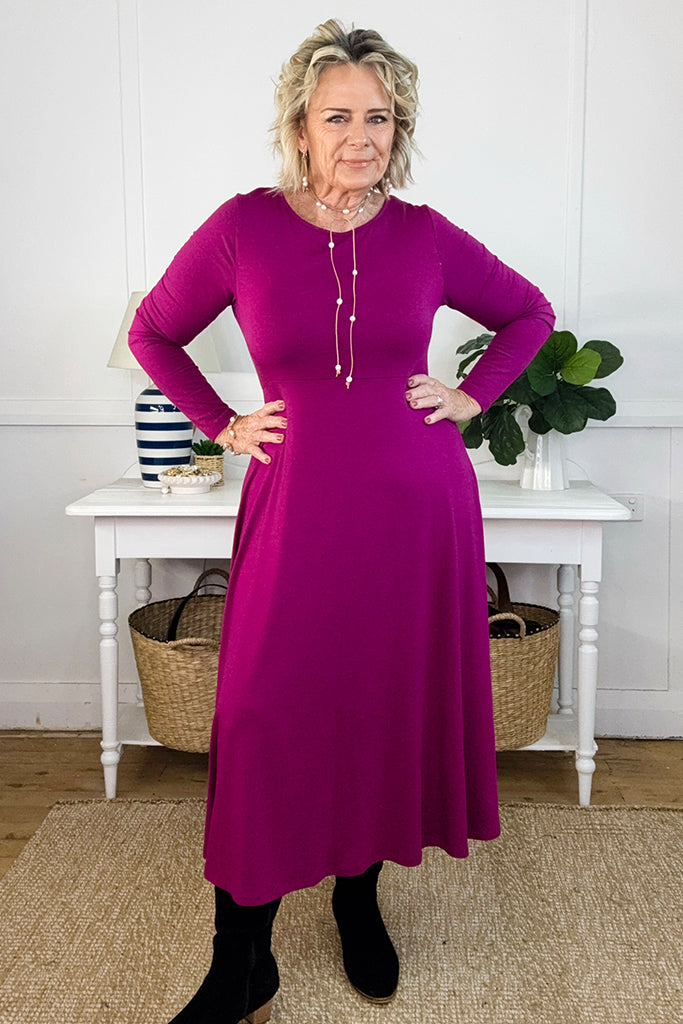 Woman wearing a purple dress standing in a room with a white table and plants.