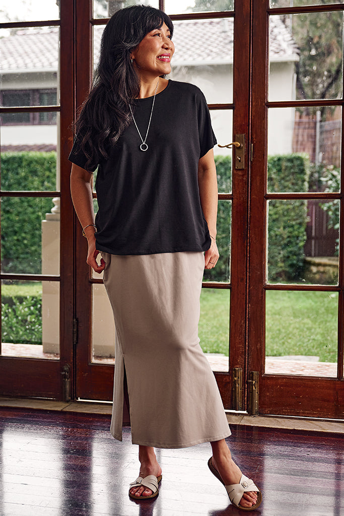 Woman wearing a black bamboo top and beige skirt standing in front of glass doors.