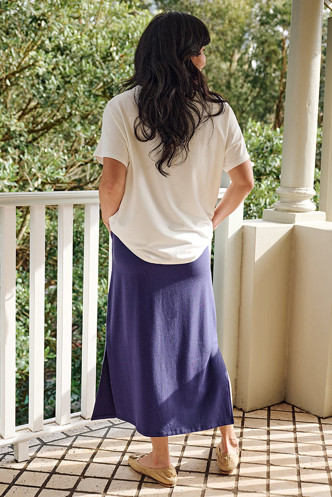 Back view of model standing on a balcony wearing a white loose top and purple skirt.