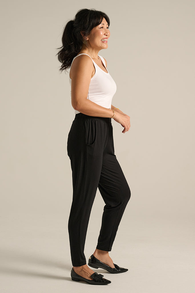 A side profile of a woman wearing the Peggy Bamboo Trouser in black, paired with a white top and black flats.