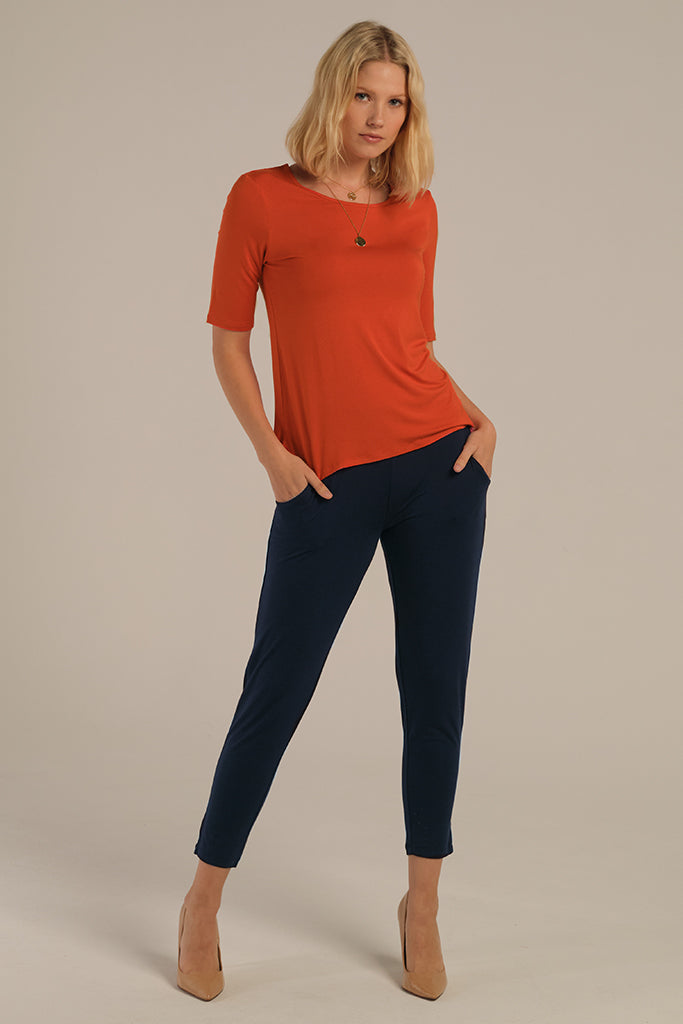 a woman wearing an outfit featuring bamboo pants with a tapered leg and side pockets in the dark navy colour paired with the orange t-shirt