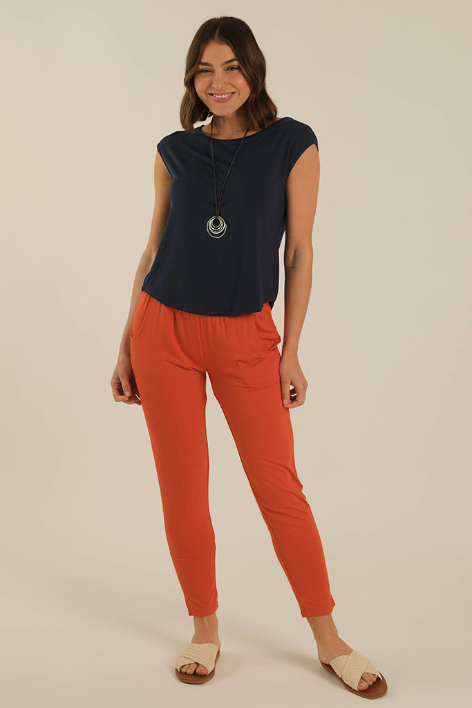 A woman wearing orange bamboo trousers with an elastic waistband and side pockets, paired with a navy top.