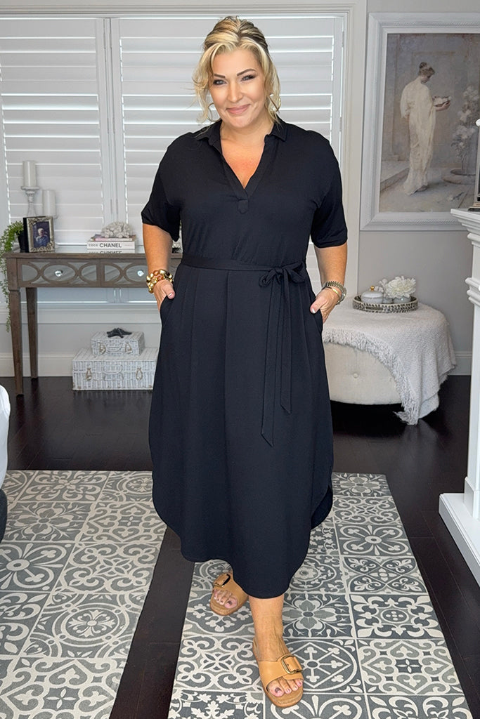 Plus size model wearing a black maxi dress with elbow length sleeves and an adjustable waist tie.