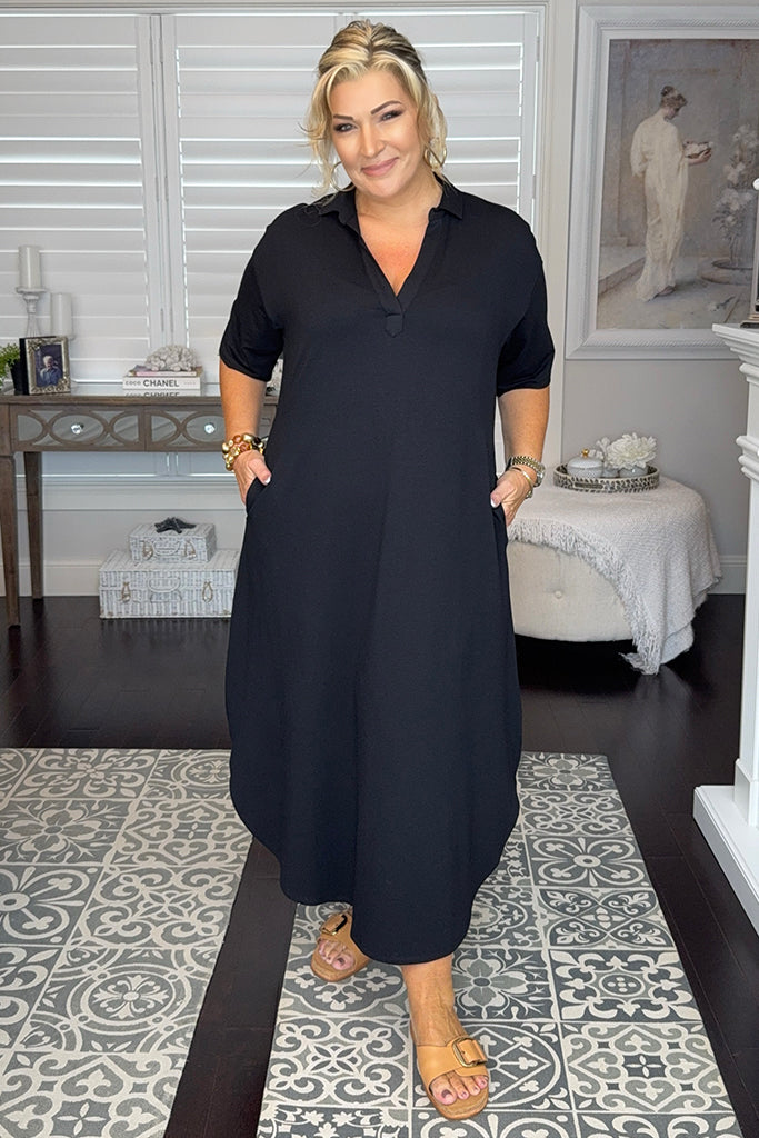 Curvy woman wearing a black maxi dress with side pockets and a v neckline.