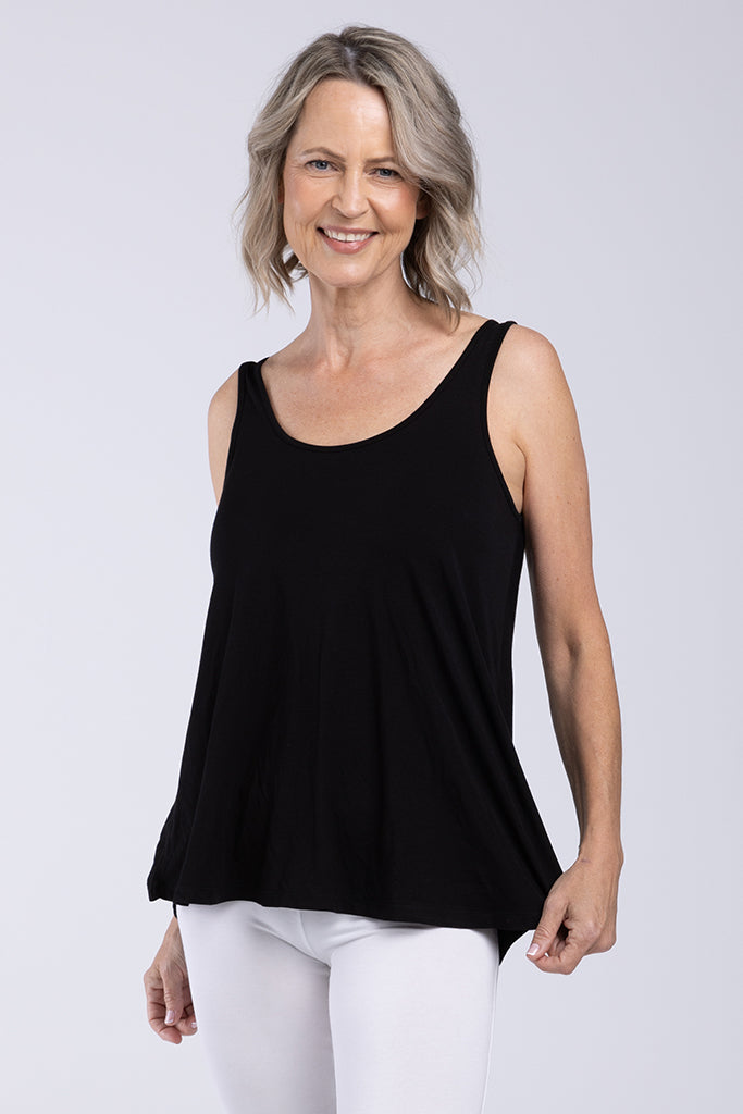 A woman wearing a black sleeveless singlet with a relaxed fit and a-line shape, paired with white trousers.