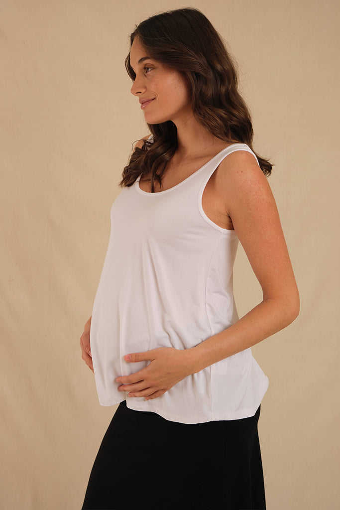 Pregnant model standing sideways wearing long white relaxed maternity singlet with lots of room for a growing belly.