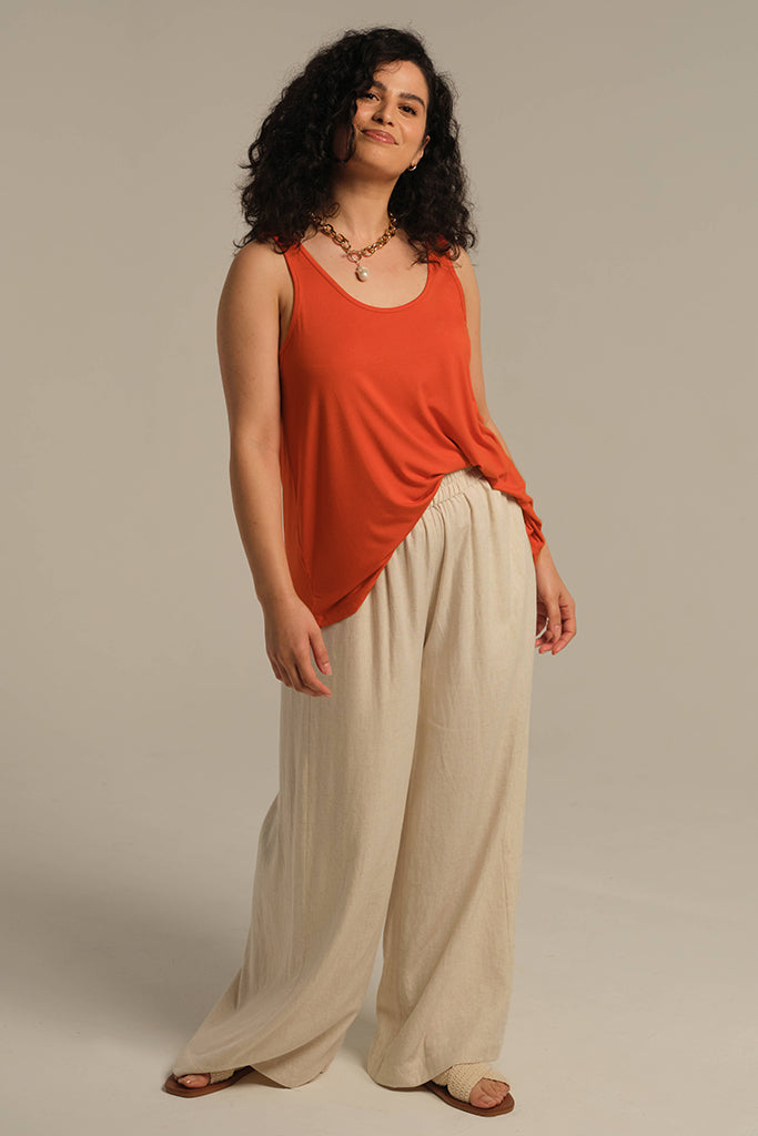 Model standing wearing orange flame singlet tucked into floaty wide leg pants to break up the look.