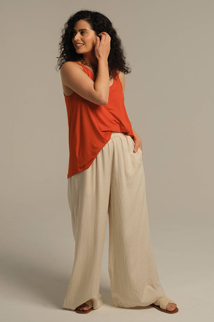 Model wearing orange loose fitted singlet with scoop neck and longer length for good coverage.