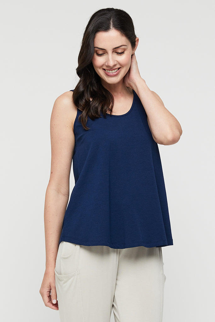 A woman wearing a navy sleeveless singlet with a relaxed fit and a-line shape, paired with light pants.