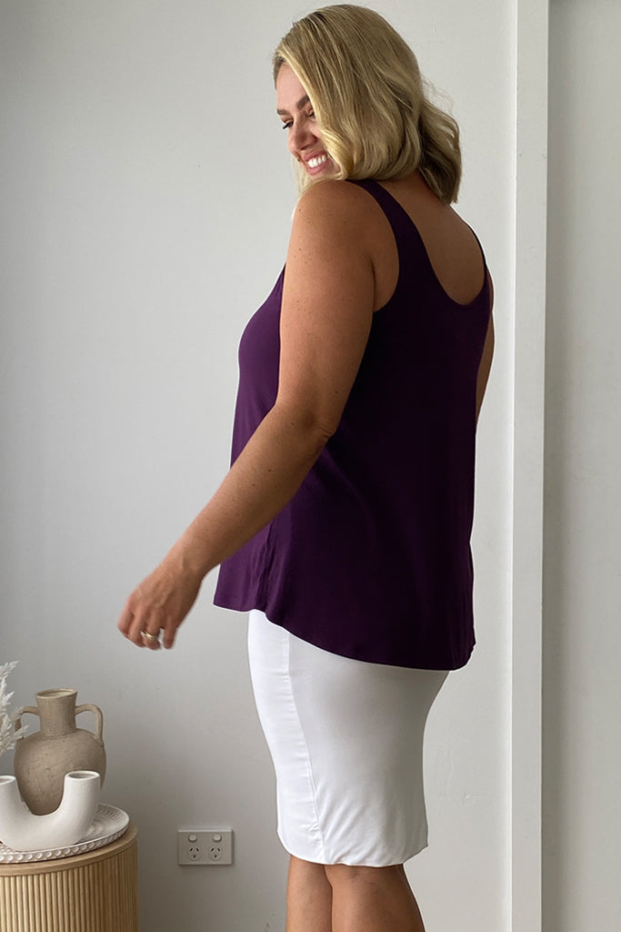 Model standing sidewards wearing a plum relaxed singlet with a curved bottom hem