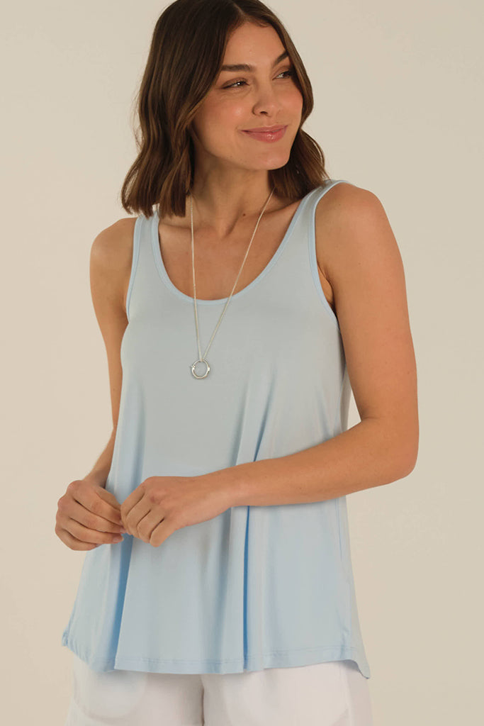 A woman wearing a sleeveless powder blue singlet with a relaxed A-line shape, paired with white pants.