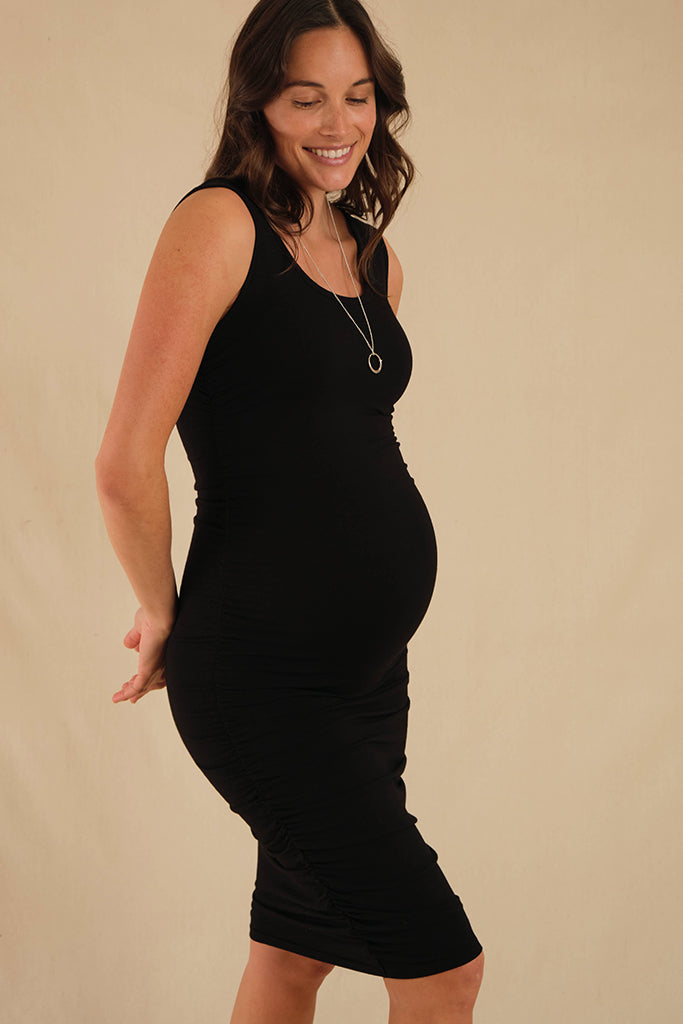 Side view of maternity dress in black featuring ruching that stretches to fit a growing belly.