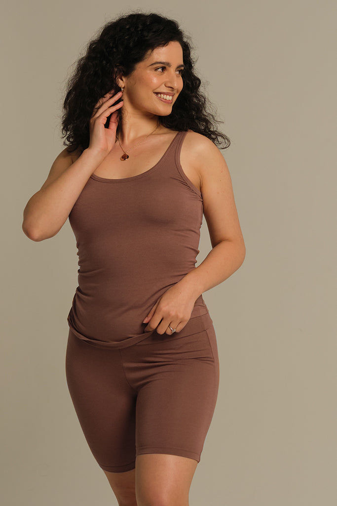 A woman wearing a brown sleeveless tank top with a scooped neckline, fitting style, and thick straps.