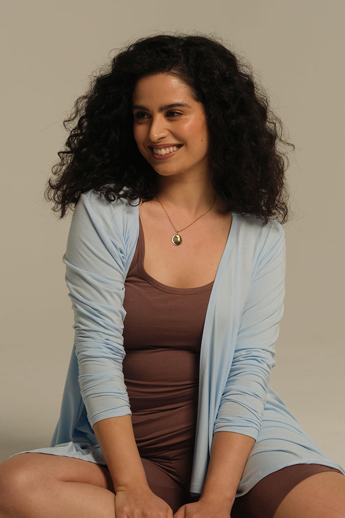 Model sitting on the floor feeling comfy wearing brown singlet with cardigan on top.