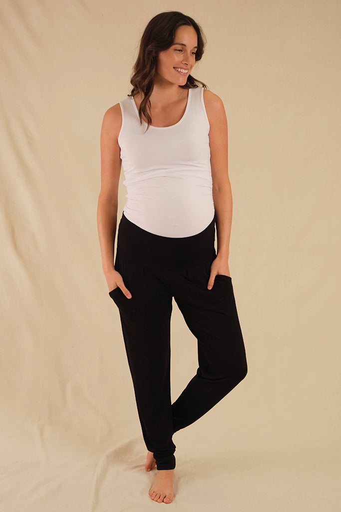 A pregnant woman wearing black slouch maternity pants with side pockets, soft strechy waistband and cuffed ankles