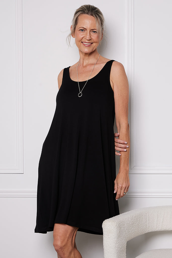 A model wearing a knee-length black sleeveless swing dress with a scoop neckline.