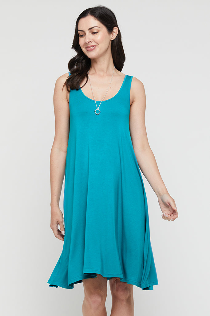 A woman wearing a knee-length teal bamboo dress with a scoop neckline and sleeveless design
