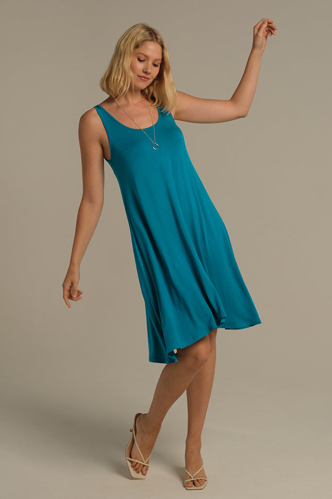 A woman wearing a knee-length sleeveless swing dress in teal color, with a scoop neckline.