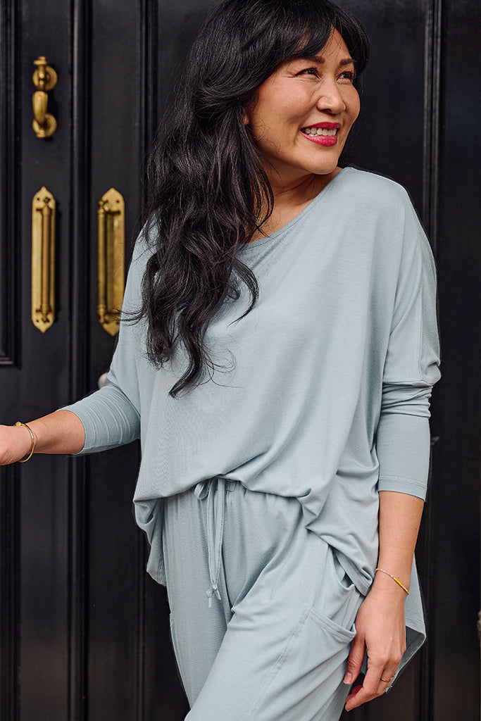 Woman wearing a light blue transit set standing in front of a dark door with gold handles.
