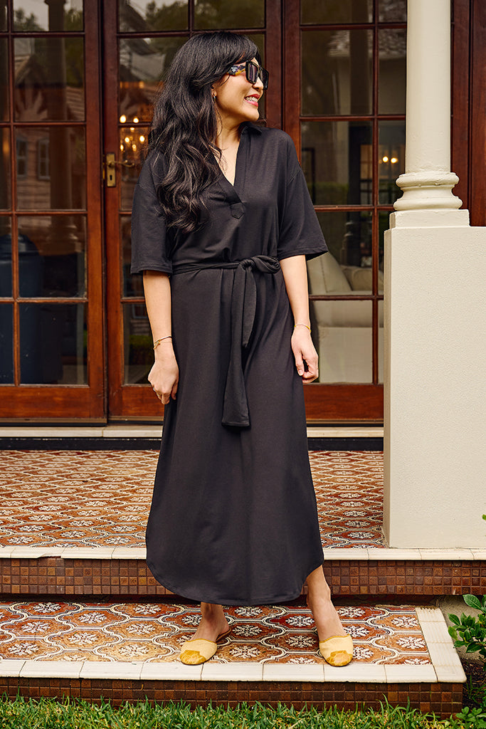 Woman wearing a black bamboo dress standing on a decorative porch.