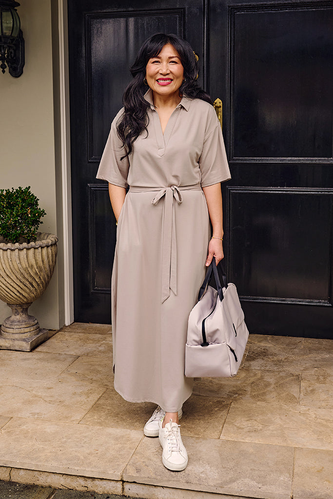 Woman in a beige oversized dress holding a grey travel bag.